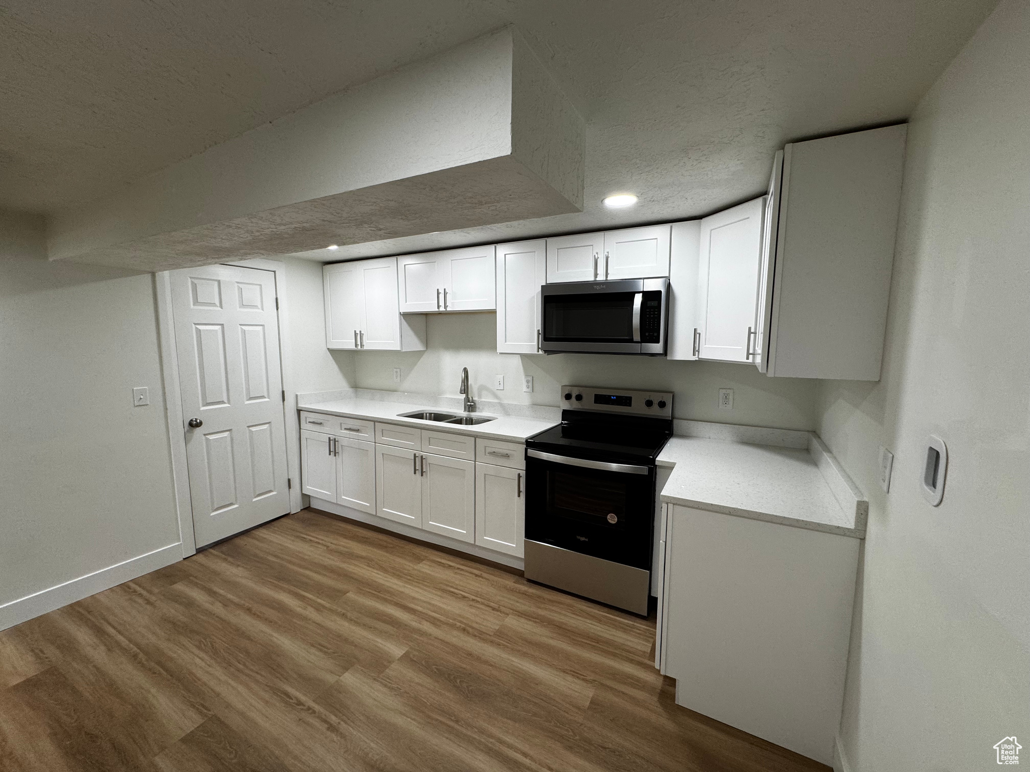 Kitchen featuring a textured ceiling, stainless steel appliances, sink, white cabinets, and light hardwood / wood-style floors