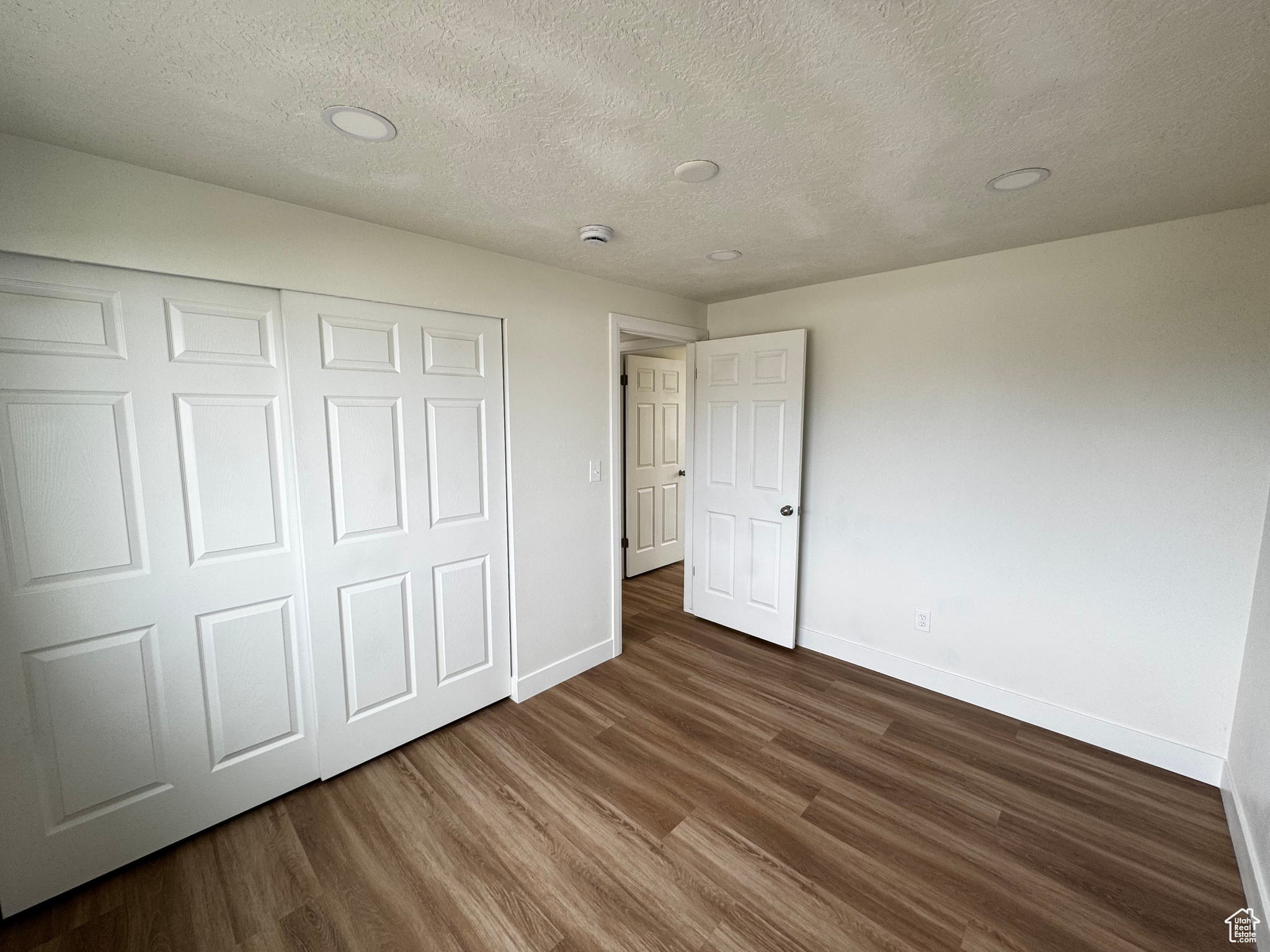 Unfurnished bedroom with a closet, dark hardwood / wood-style flooring, and a textured ceiling