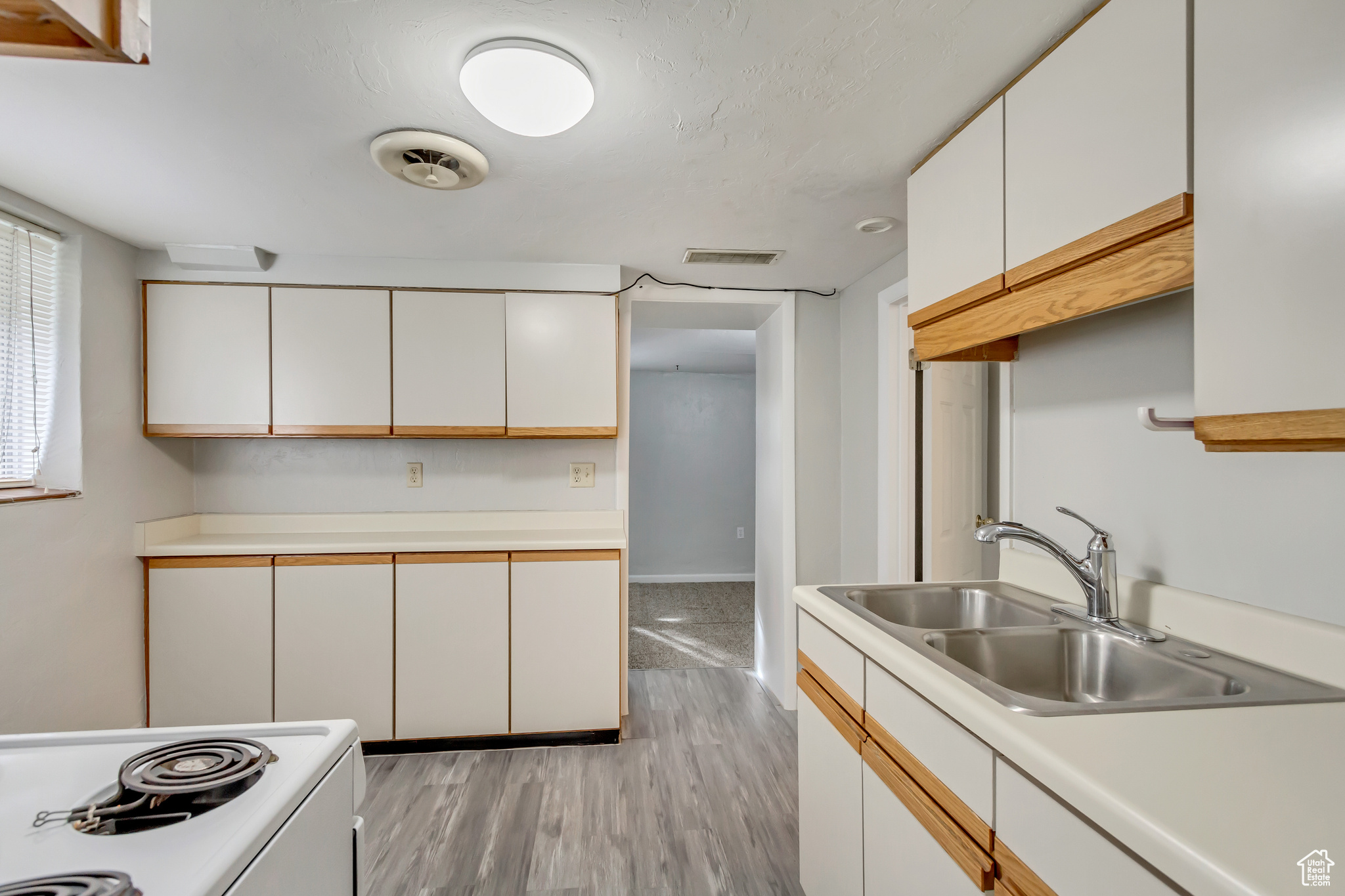 Kitchen with white range with electric cooktop, light hardwood / wood-style floors, white cabinetry, and sink