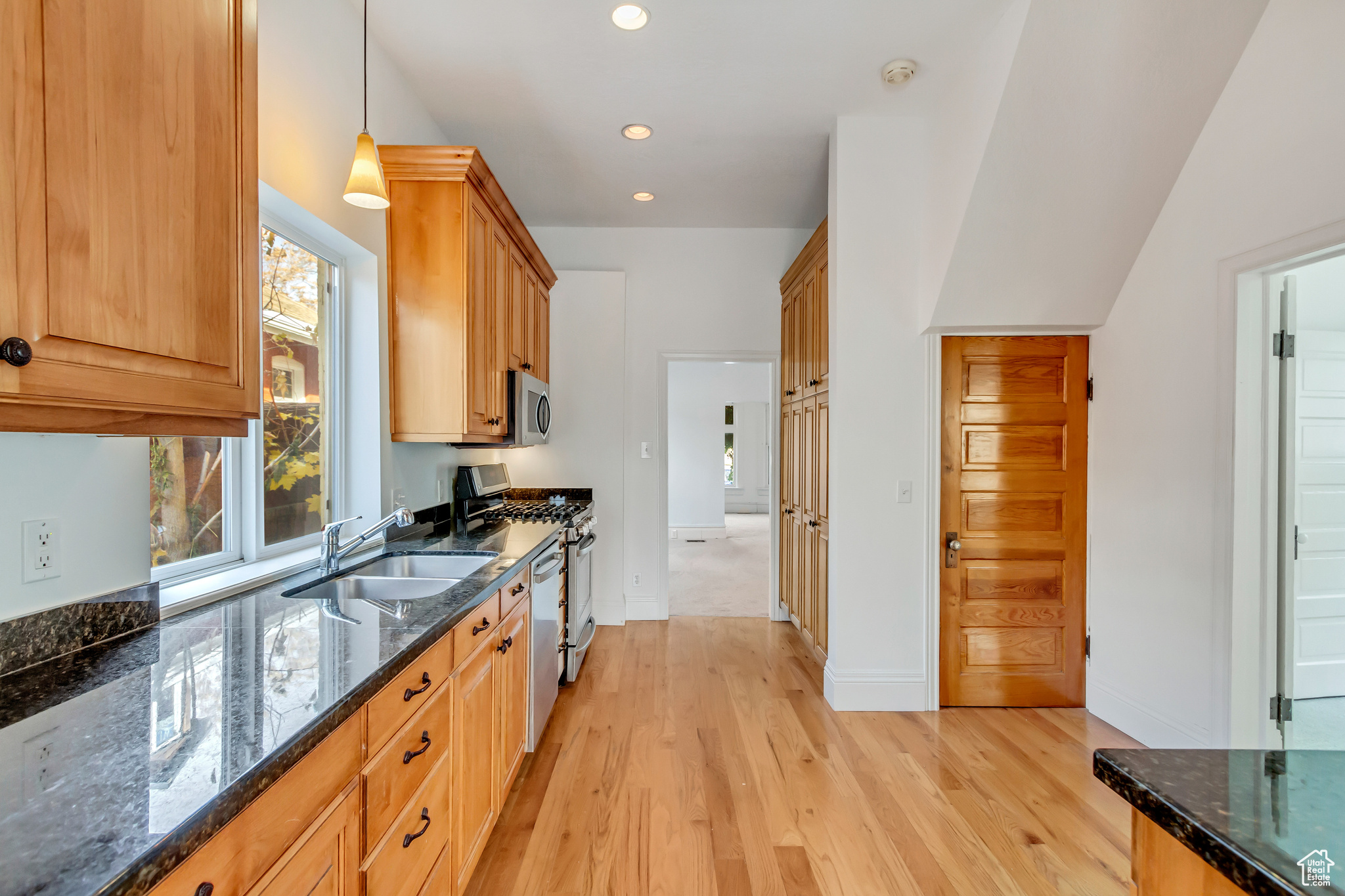 Kitchen featuring dark stone countertops, sink, stainless steel appliances, and light wood-type flooring