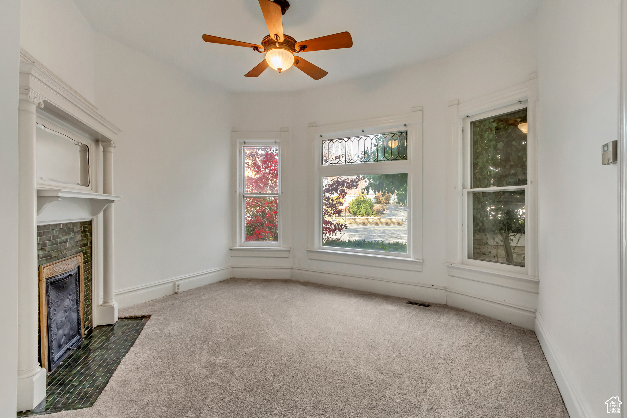 Unfurnished living room featuring ceiling fan, dark carpet, and a brick fireplace