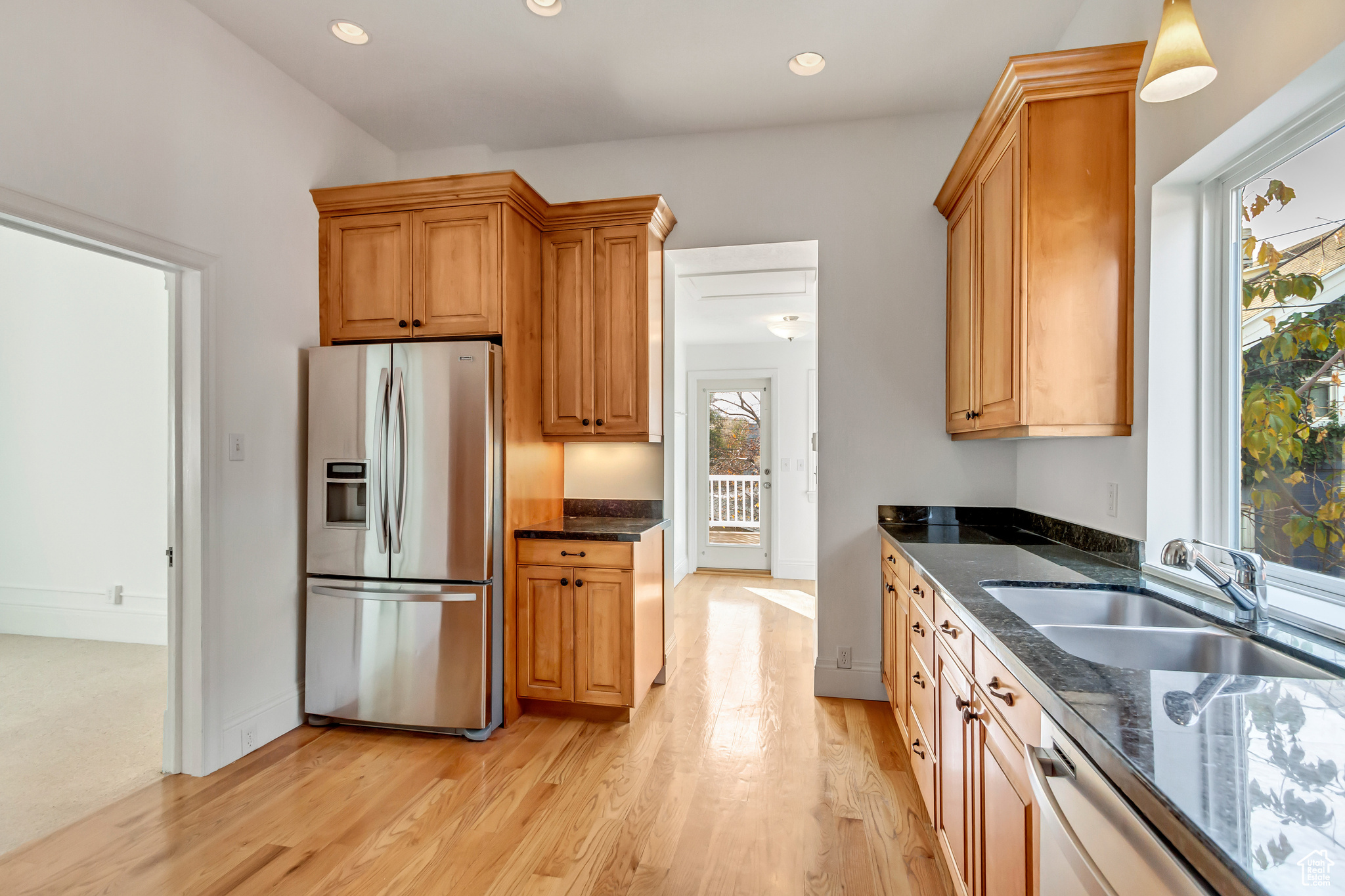 Kitchen featuring appliances with stainless steel finishes, dark stone counters, sink, decorative light fixtures, and light hardwood / wood-style floors