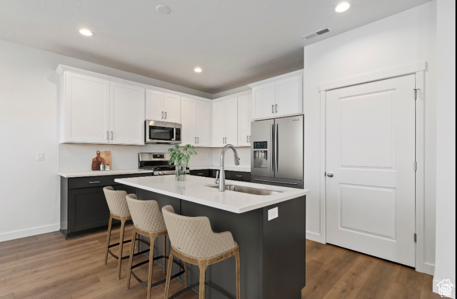 Kitchen featuring stainless steel appliances, dark wood-type flooring, sink, white cabinets, and an island with sink