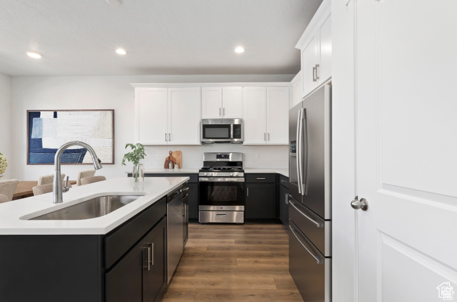 Kitchen with a kitchen island with sink, sink, appliances with stainless steel finishes, dark hardwood / wood-style flooring, and white cabinetry