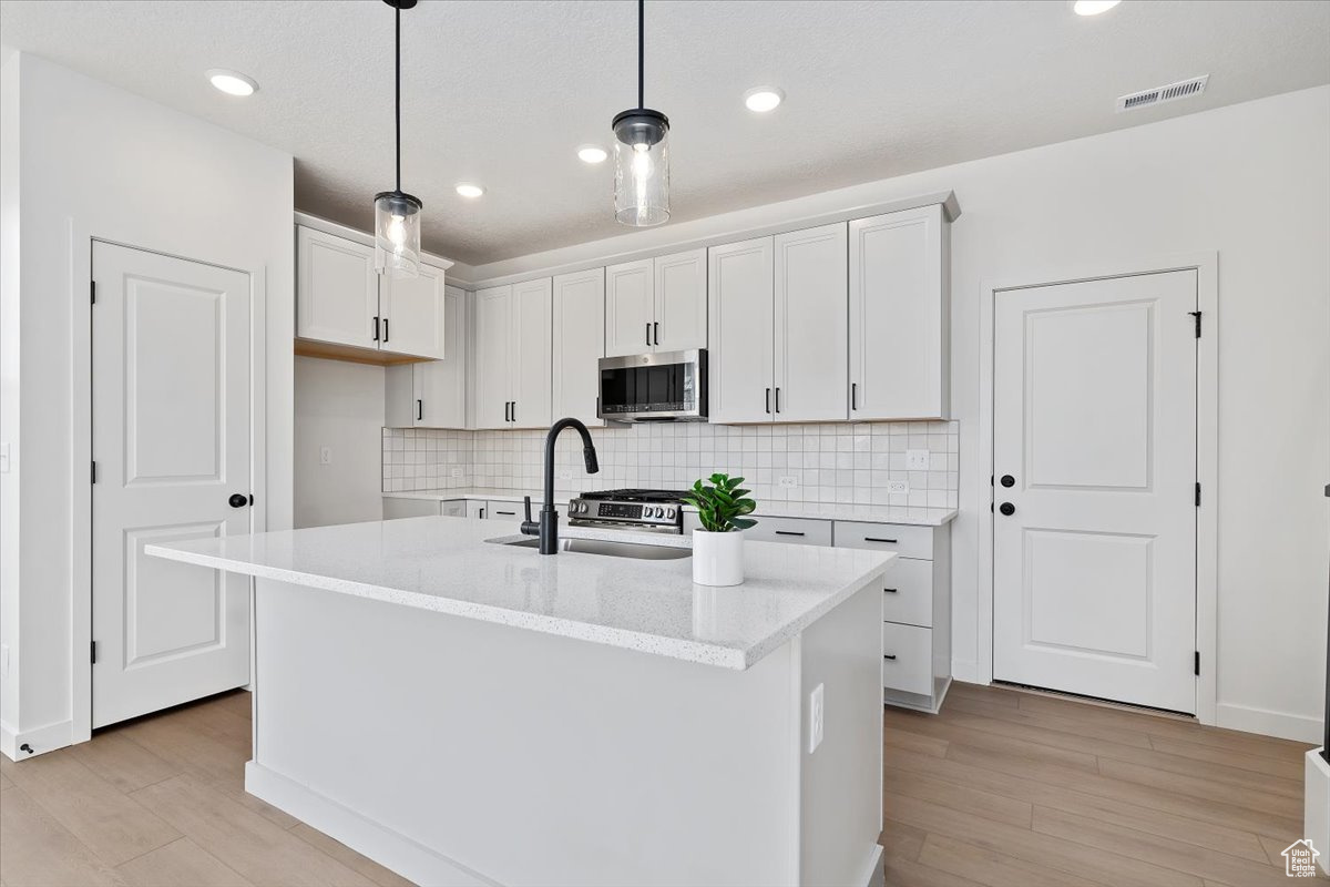 Kitchen with pendant lighting, white cabinets, sink, light hardwood / wood-style flooring, and an island with sink