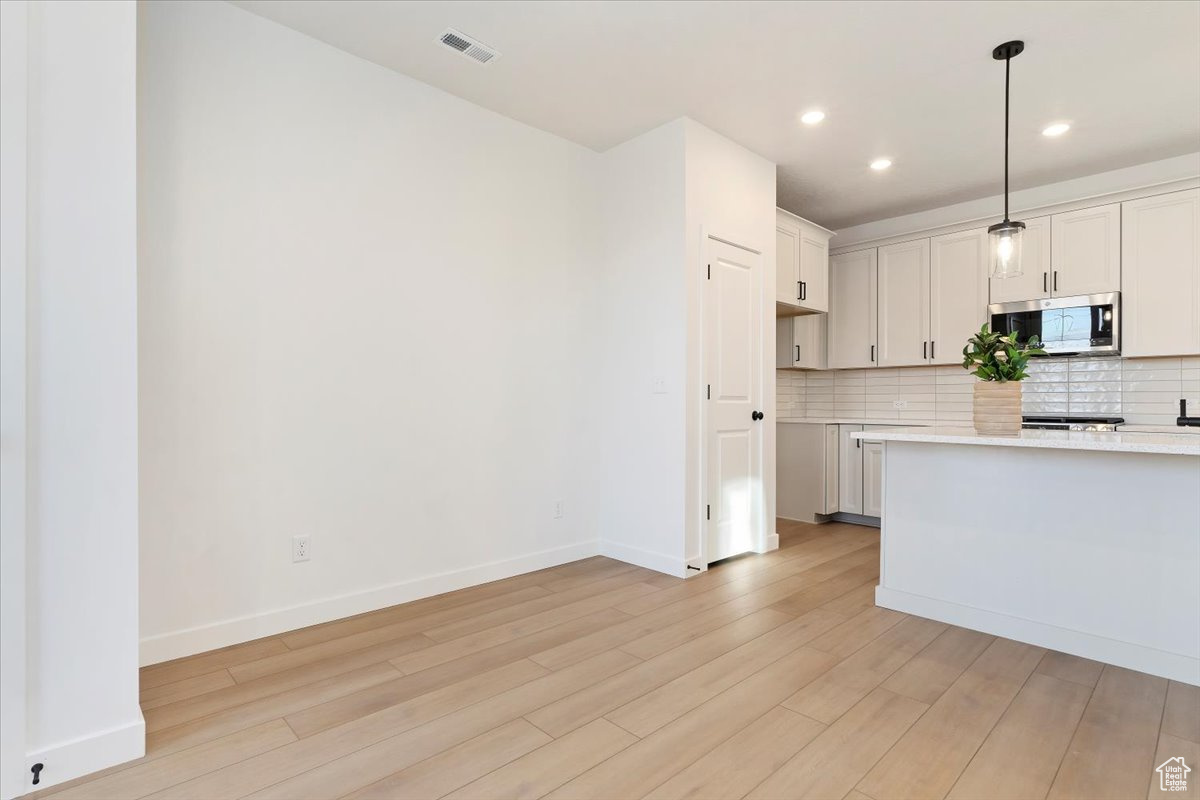 Kitchen with tasteful backsplash, white cabinets, decorative light fixtures, and light wood-type flooring