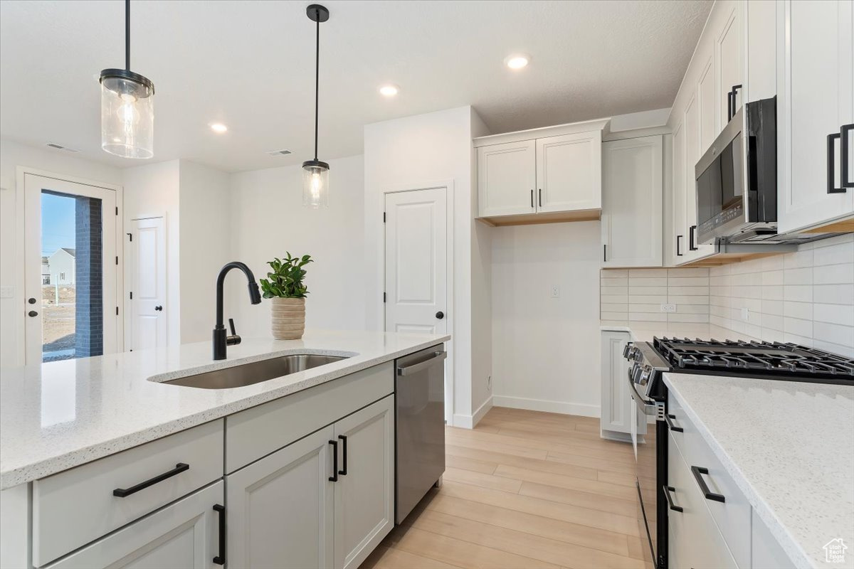 Kitchen featuring white cabinetry, sink, light stone counters, pendant lighting, and appliances with stainless steel finishes