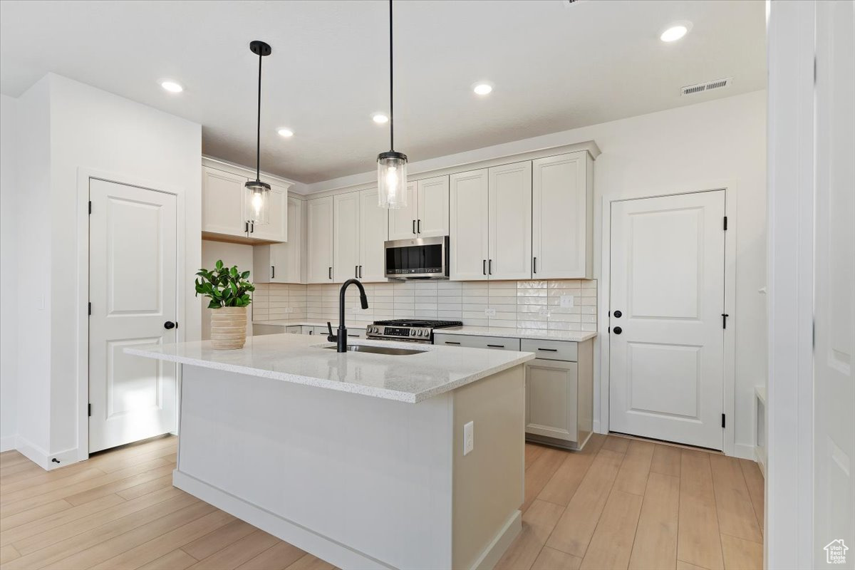 Kitchen featuring a kitchen island with sink, sink, light stone counters, and decorative light fixtures