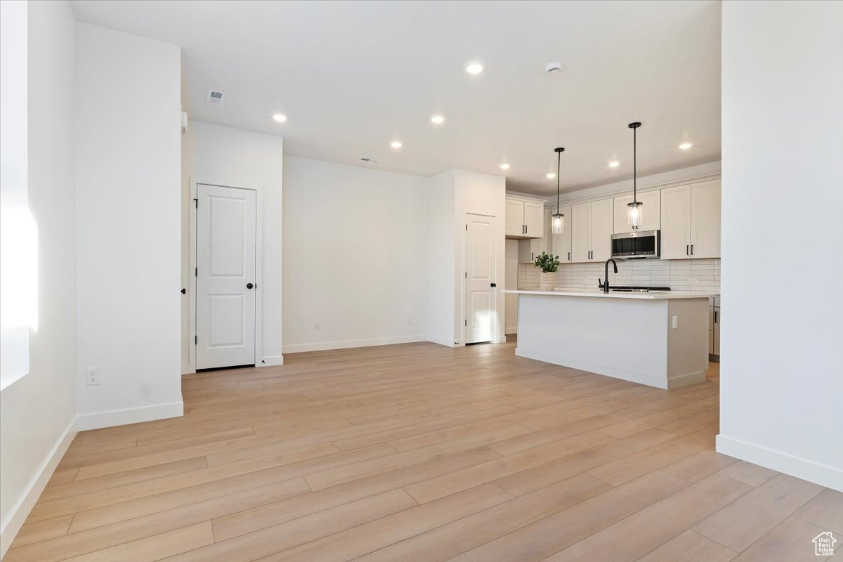 Kitchen with backsplash, a center island with sink, light hardwood / wood-style floors, white cabinetry, and hanging light fixtures