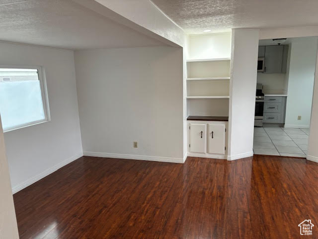 Unfurnished living room with hardwood / wood-style floors, built in features, and a textured ceiling