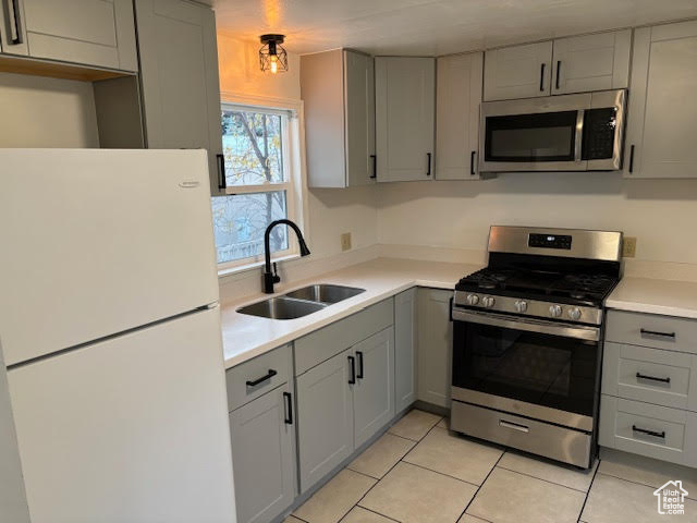 Kitchen featuring light tile patterned floors, stainless steel appliances, gray cabinets, and sink