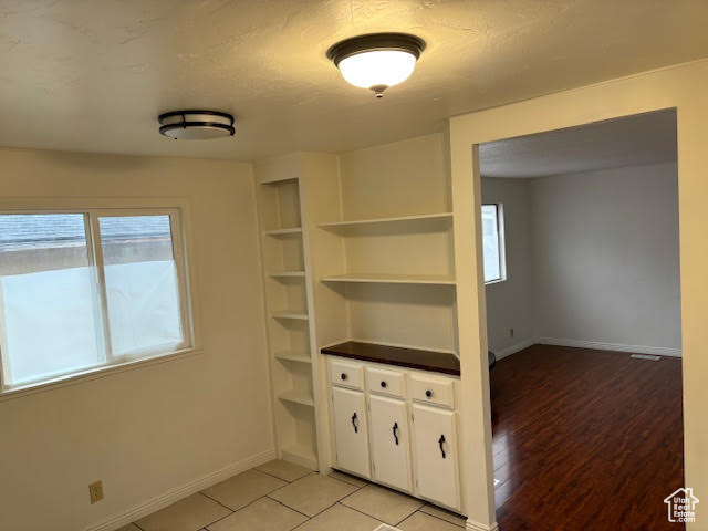 Interior space with built in shelves, a textured ceiling, and light hardwood / wood-style flooring