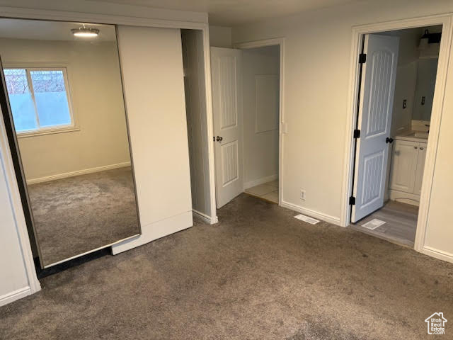 Unfurnished bedroom with ensuite bathroom, dark carpet, and a closet