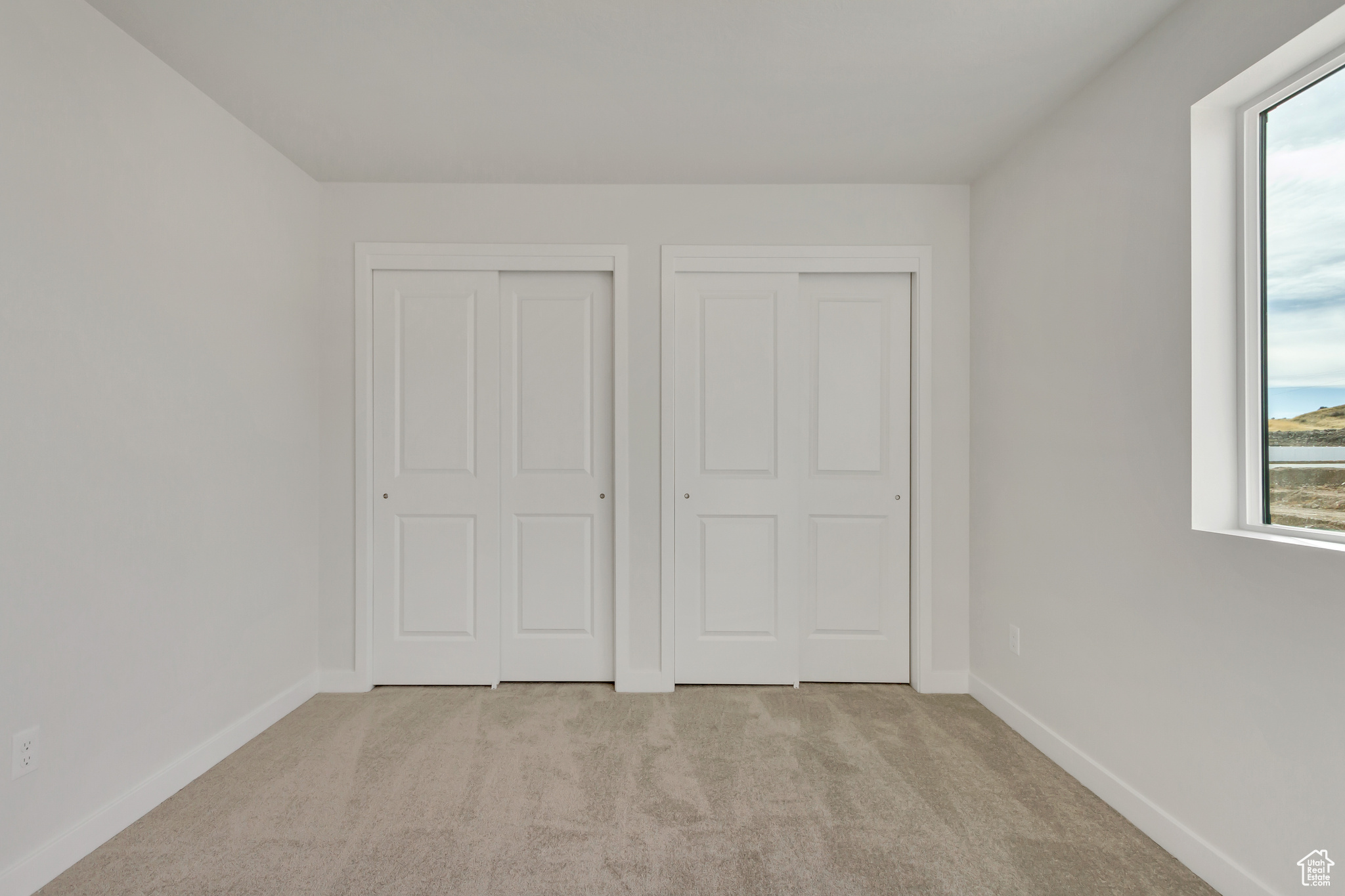 Unfurnished bedroom with light colored carpet and two closets