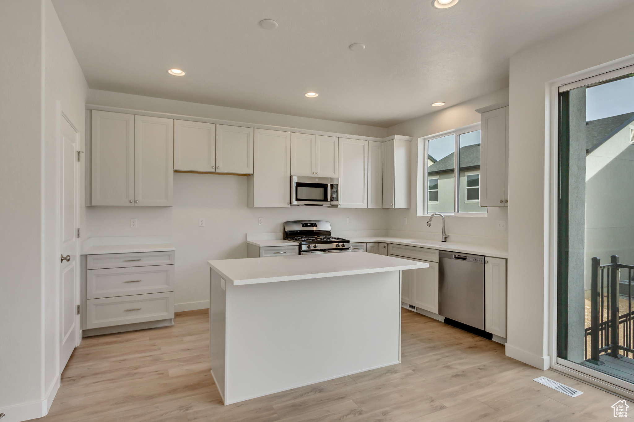 Kitchen featuring white cabinets, appliances with stainless steel finishes, light wood-type flooring, and a kitchen island