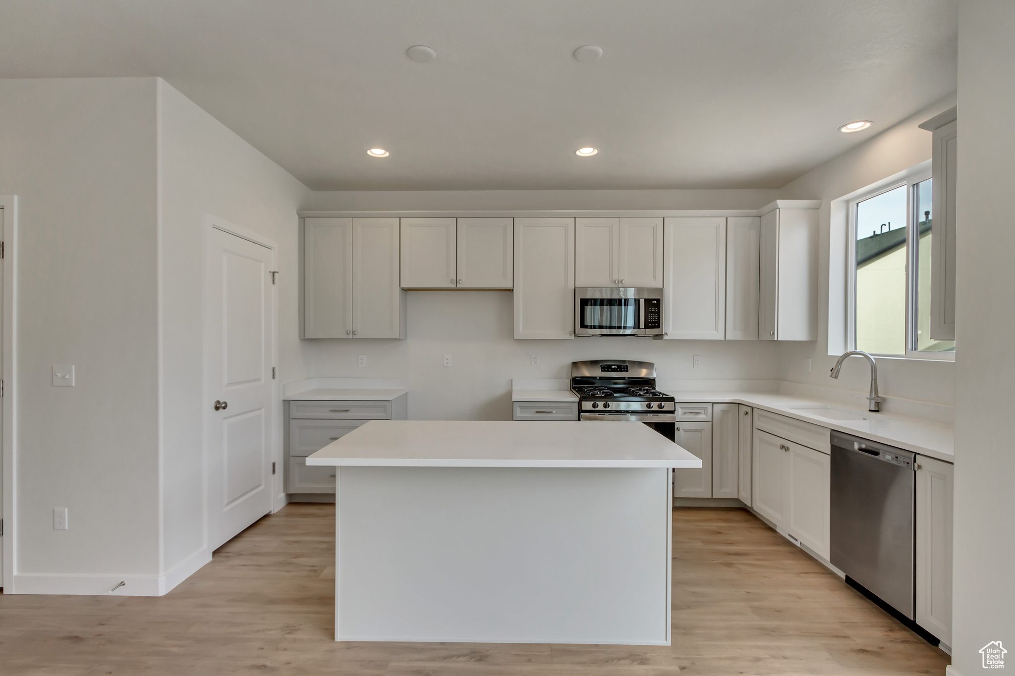 Kitchen featuring white cabinets, sink, light hardwood / wood-style flooring, a kitchen island, and stainless steel appliances