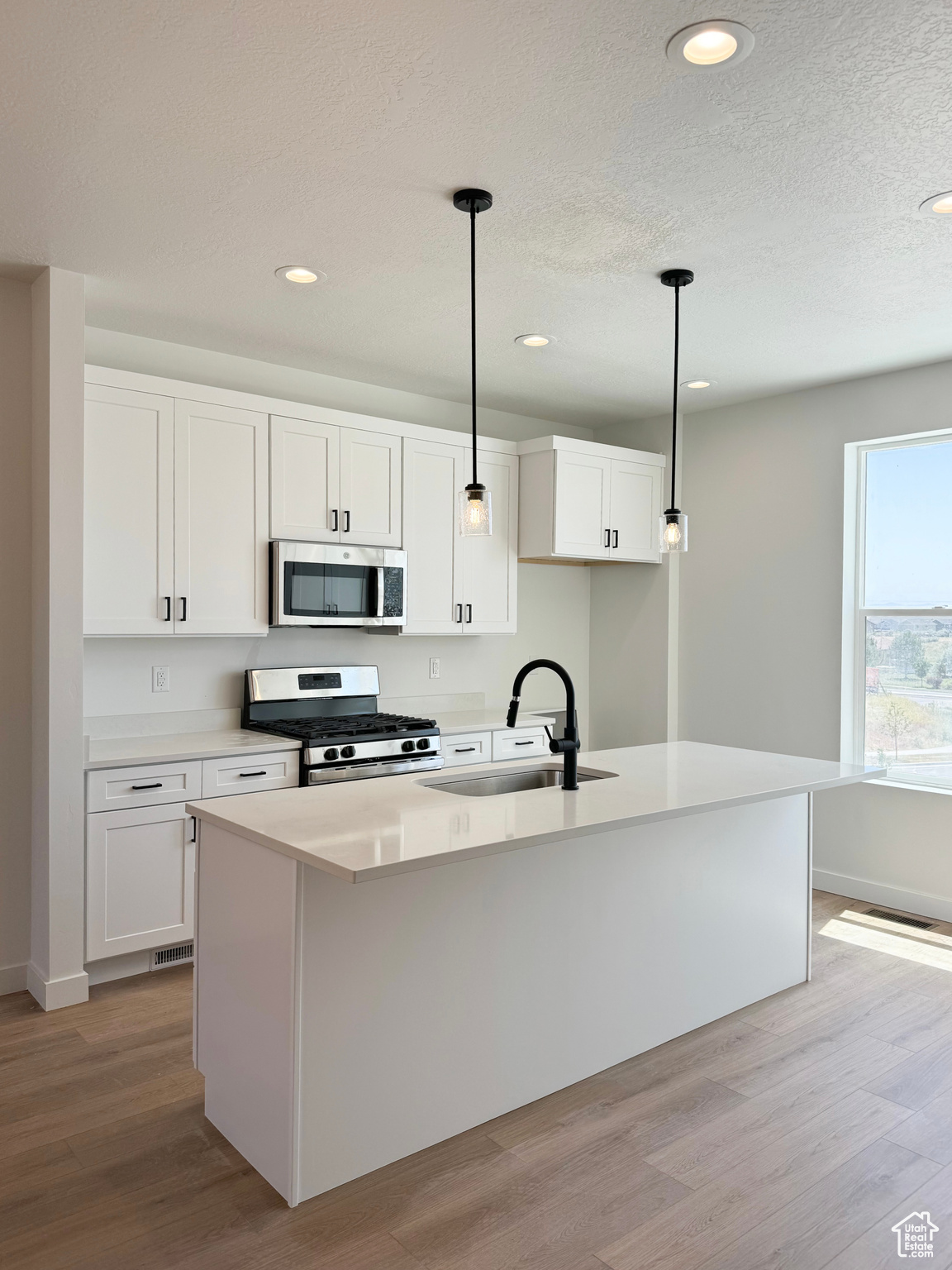 Kitchen with a kitchen island with sink, white cabinetry, sink, and appliances with stainless steel finishes