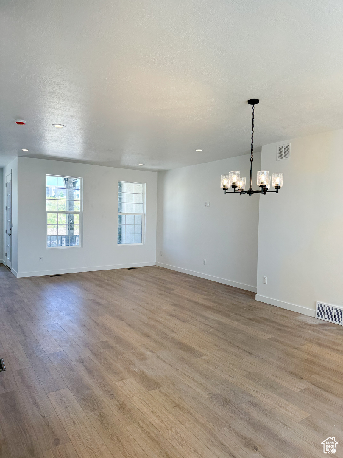 Spare room with light hardwood / wood-style floors and an inviting chandelier