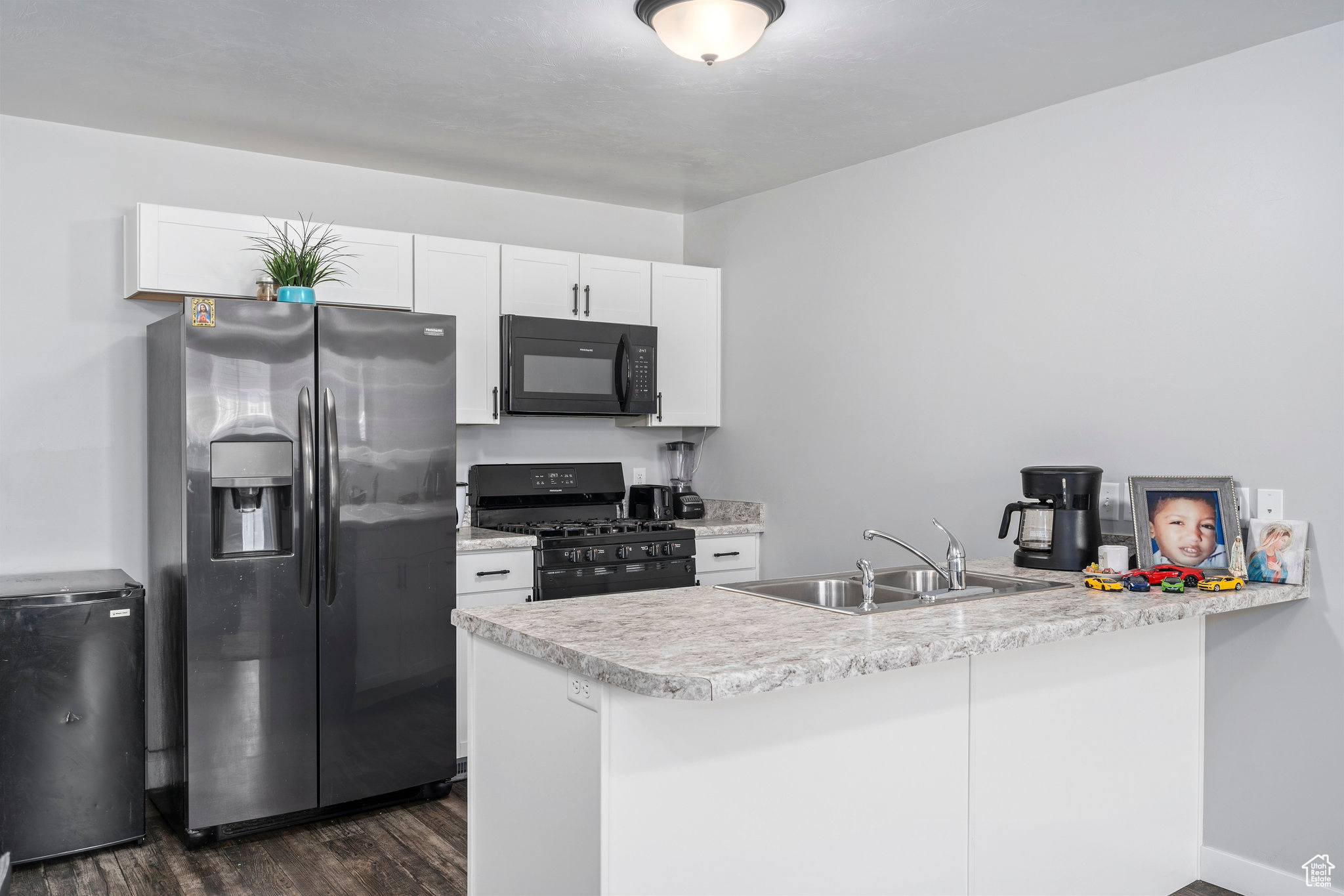 Kitchen featuring kitchen peninsula, sink, black appliances, dark hardwood / wood-style floors, and white cabinetry