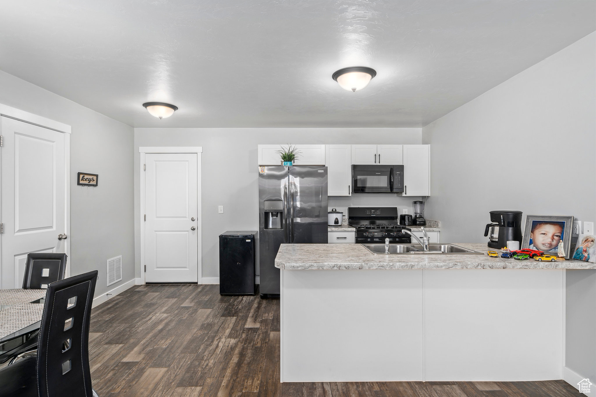 Kitchen with kitchen peninsula, dark hardwood / wood-style flooring, sink, black appliances, and white cabinets