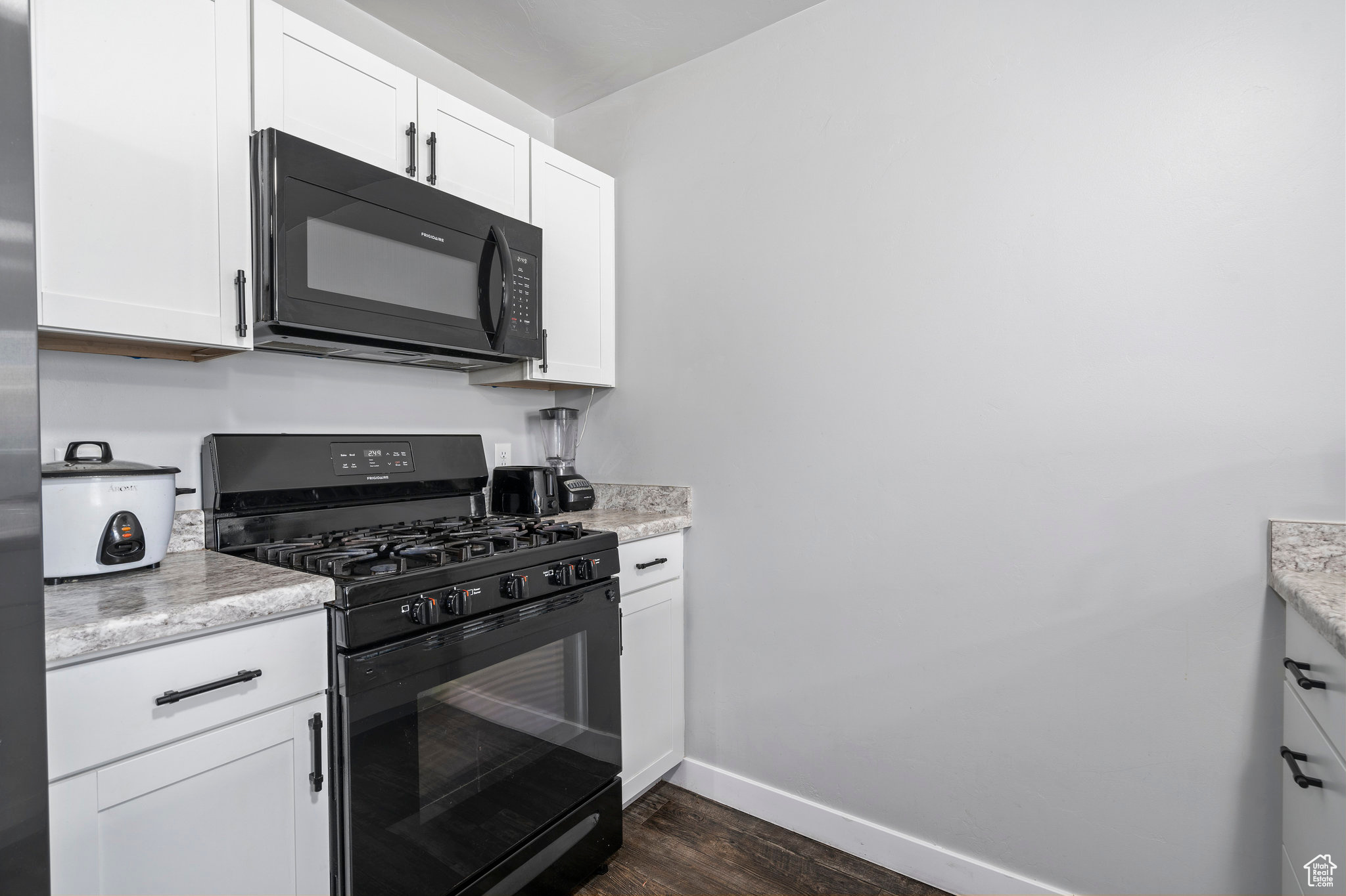 Kitchen featuring light stone counters, dark hardwood / wood-style floors, white cabinetry, and black appliances