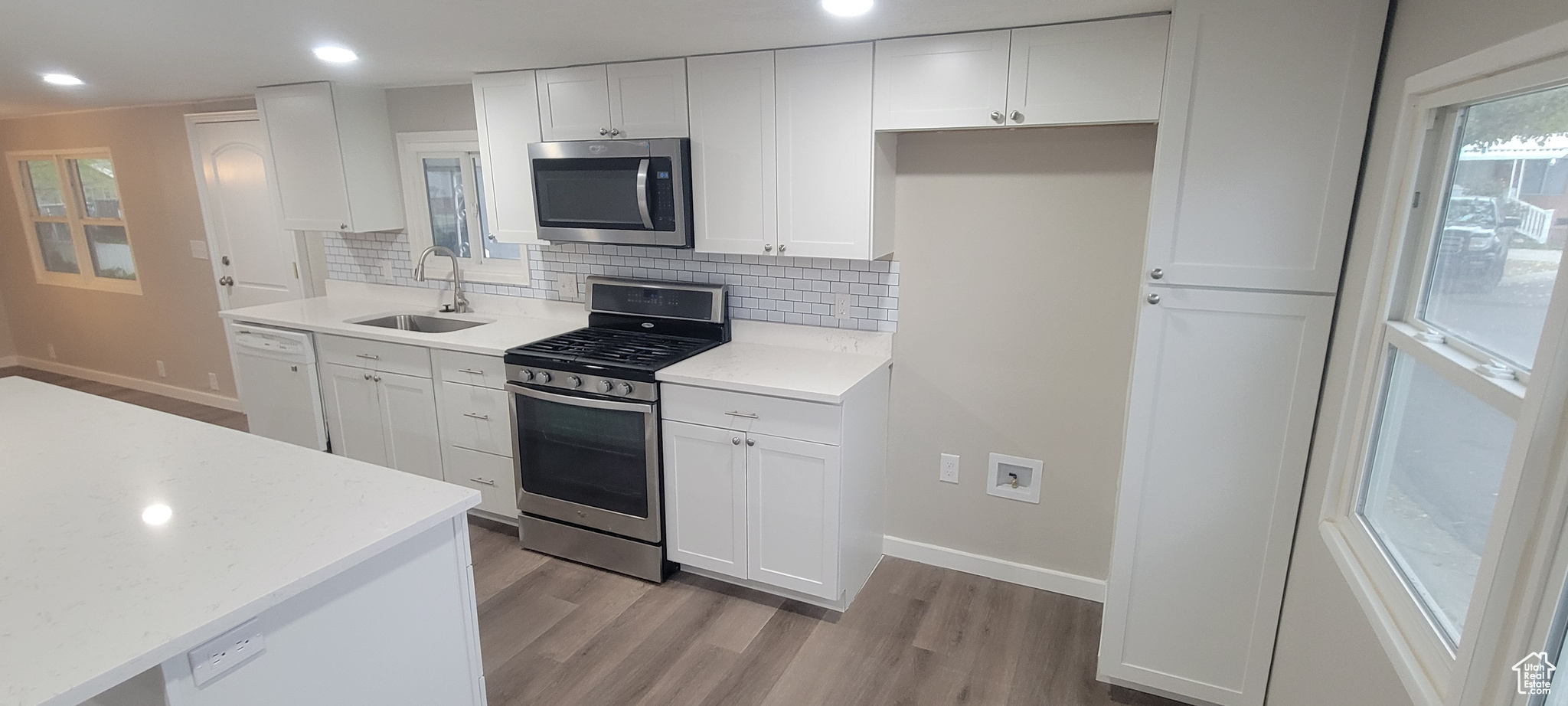 Kitchen with sink, light hardwood / wood-style flooring, decorative backsplash, white cabinets, and appliances with stainless steel finishes