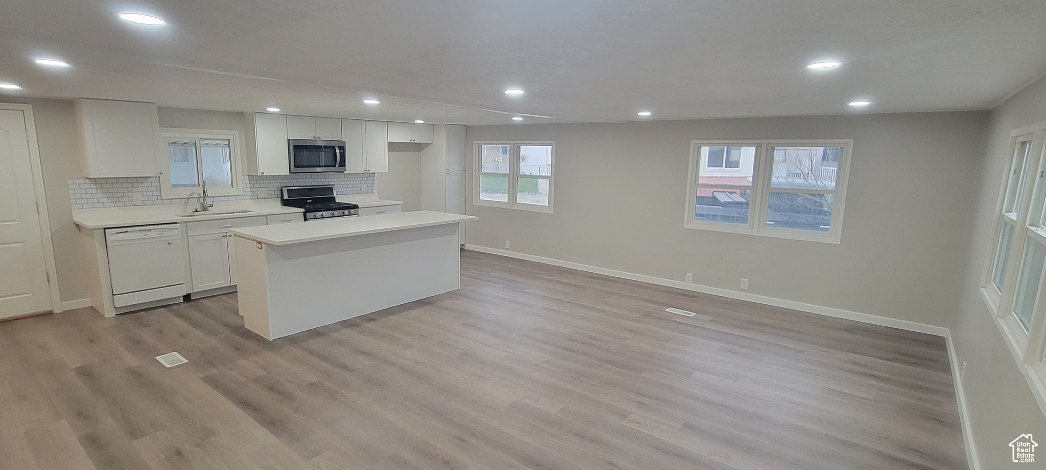 Kitchen with white cabinetry, light hardwood / wood-style flooring, a kitchen island, and appliances with stainless steel finishes