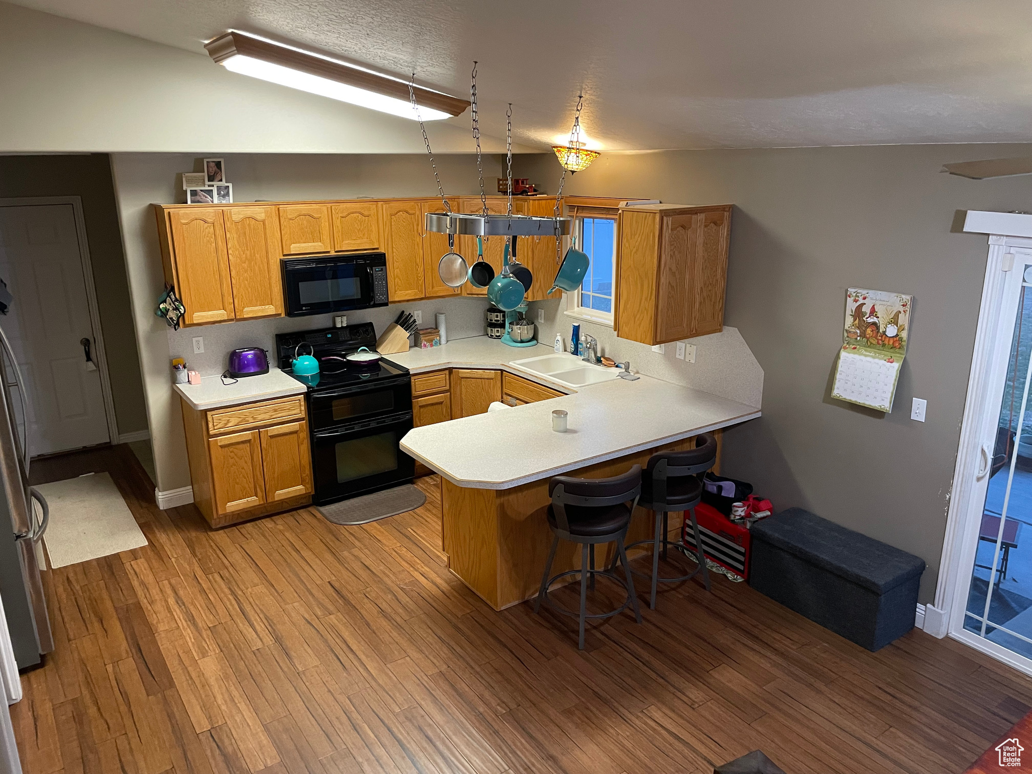 Kitchen featuring sink, kitchen peninsula, lofted ceiling, black appliances, and light wood-type flooring