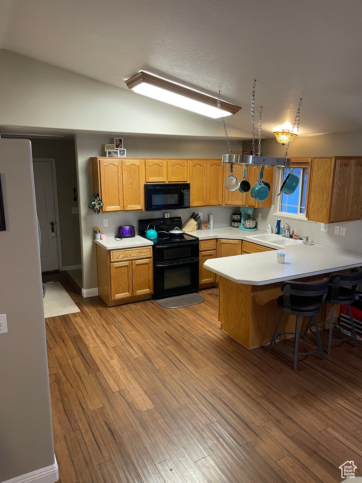 Kitchen featuring kitchen peninsula, vaulted ceiling, sink, black appliances, and light hardwood / wood-style floors