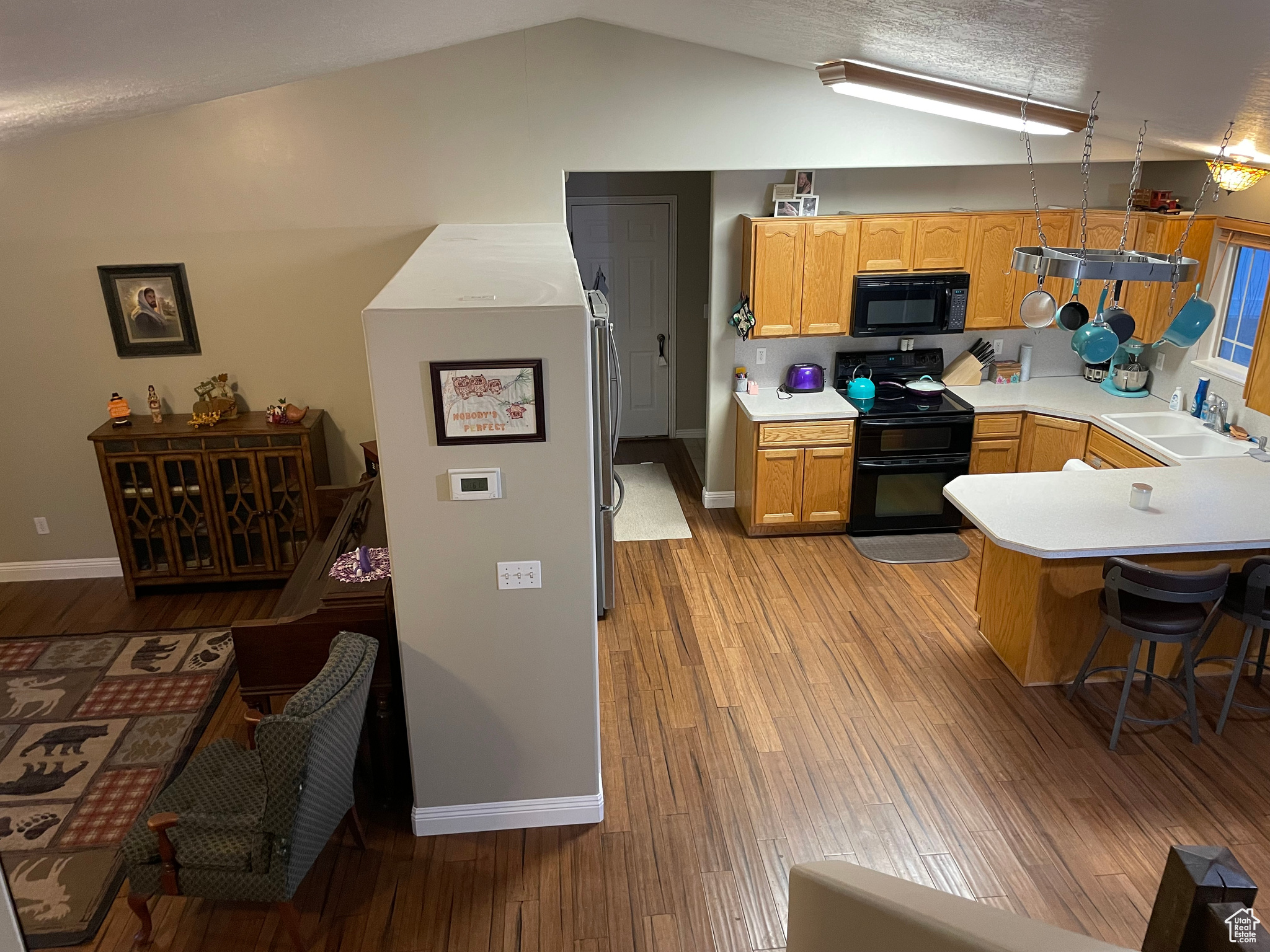 Kitchen featuring sink, black appliances, lofted ceiling, and light wood-type flooring