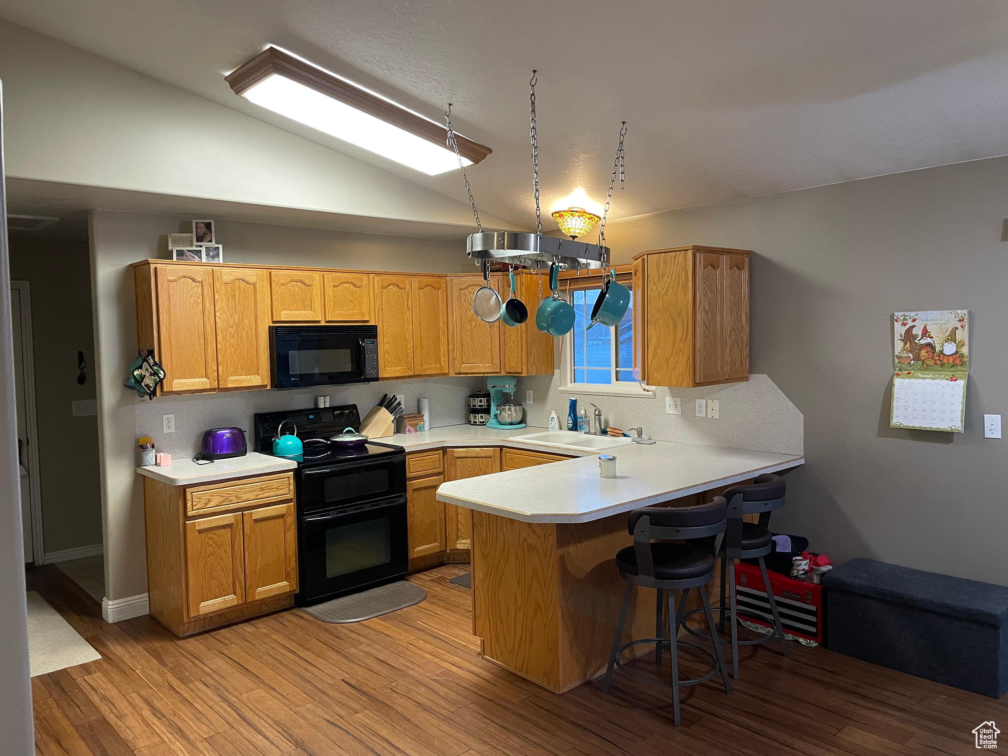 Kitchen featuring kitchen peninsula, vaulted ceiling, sink, black appliances, and light hardwood / wood-style floors