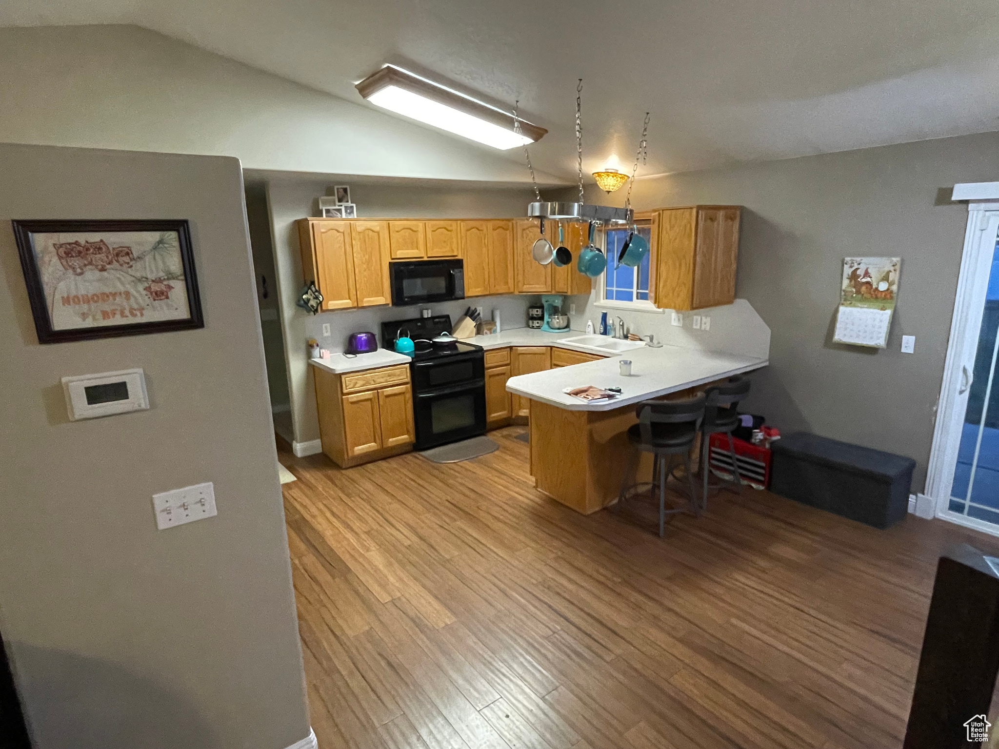 Kitchen featuring a breakfast bar, black appliances, vaulted ceiling, light hardwood / wood-style floors, and kitchen peninsula