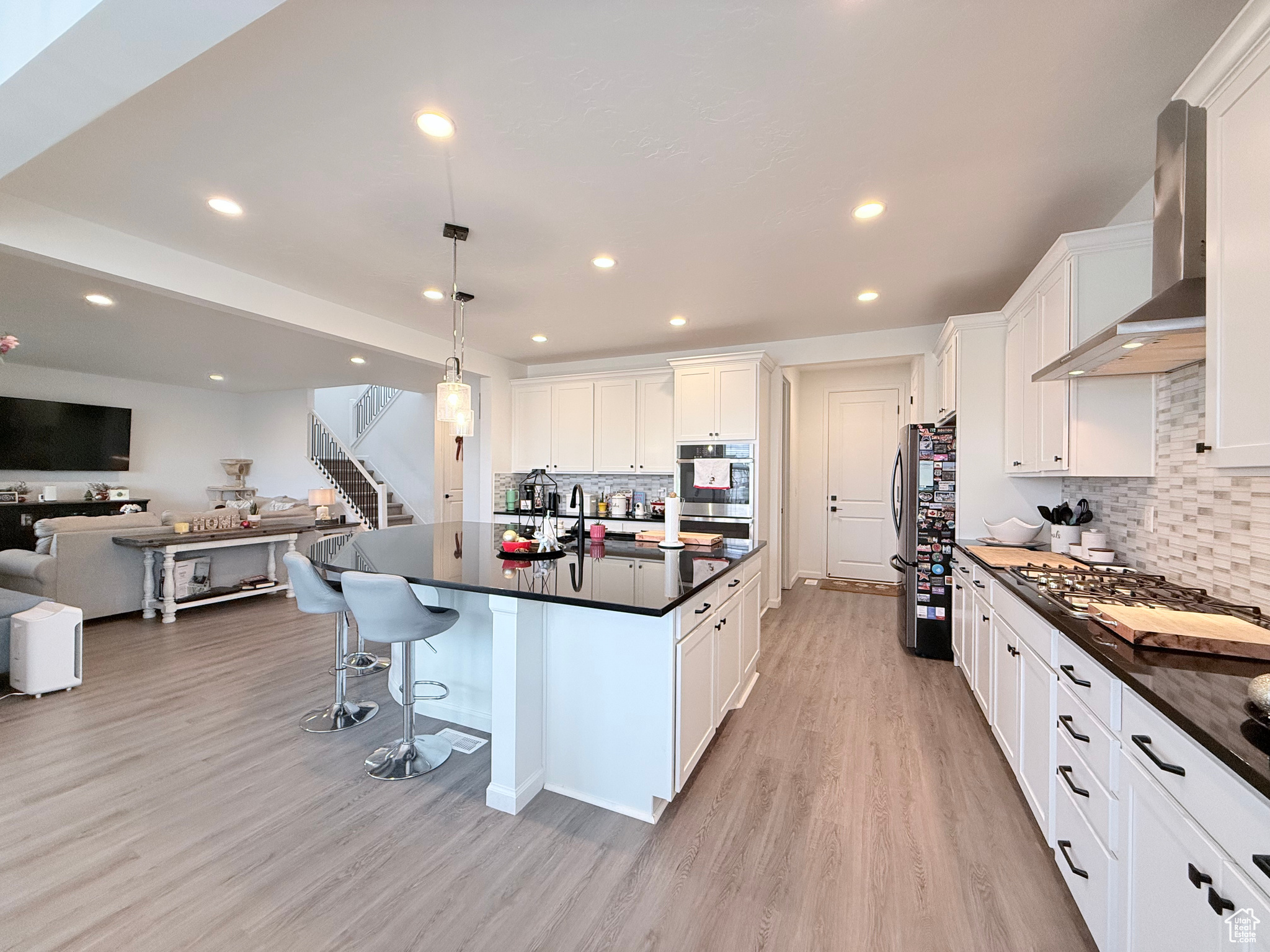 Kitchen featuring pendant lighting, stainless steel range hood, gas stovetop, black/SS appliances, double oven, and white cabinetry