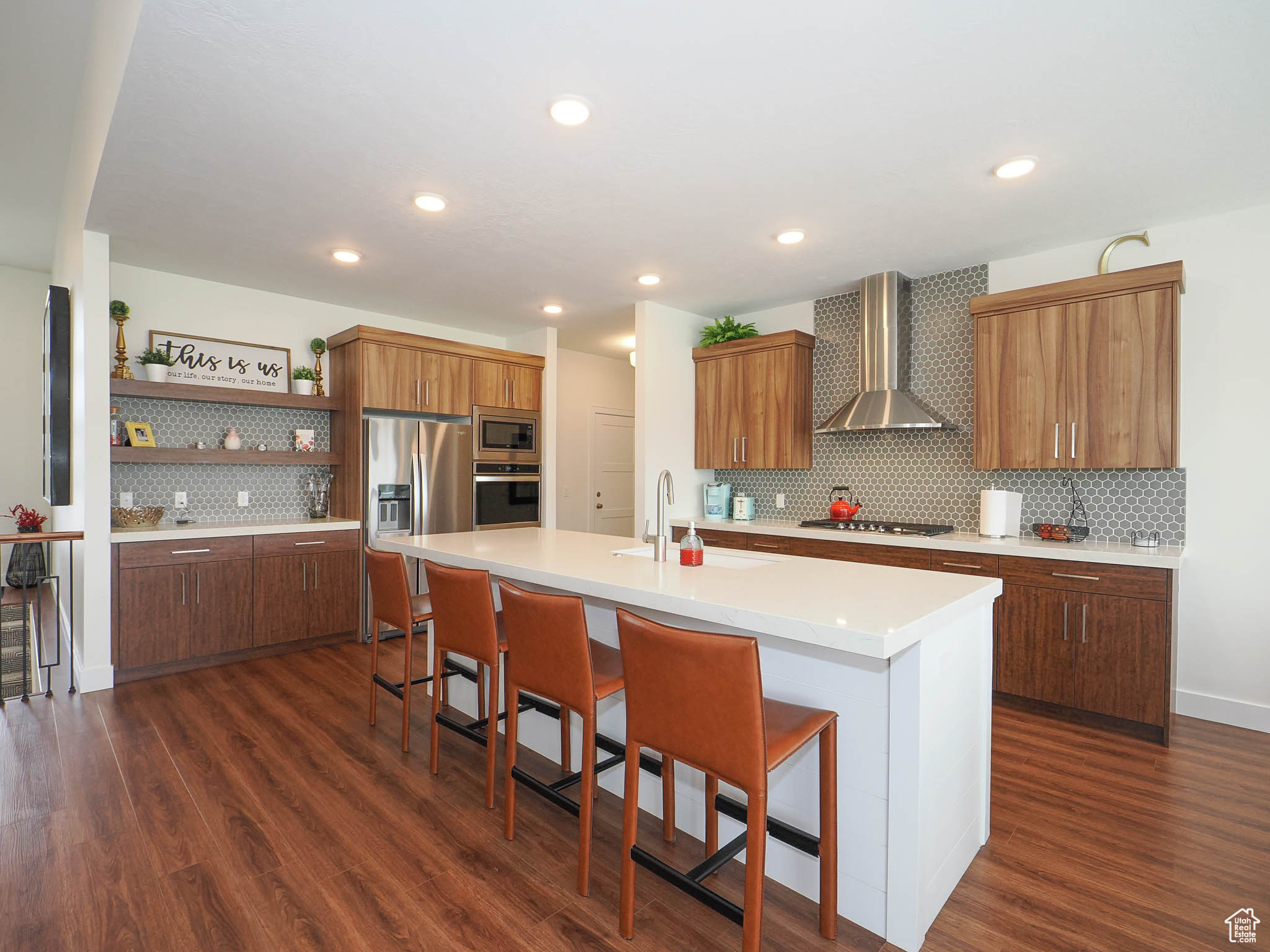 Kitchen featuring appliances with stainless steel finishes, wall chimney exhaust hood, sink, a center island with sink, and dark hardwood / wood-style floors