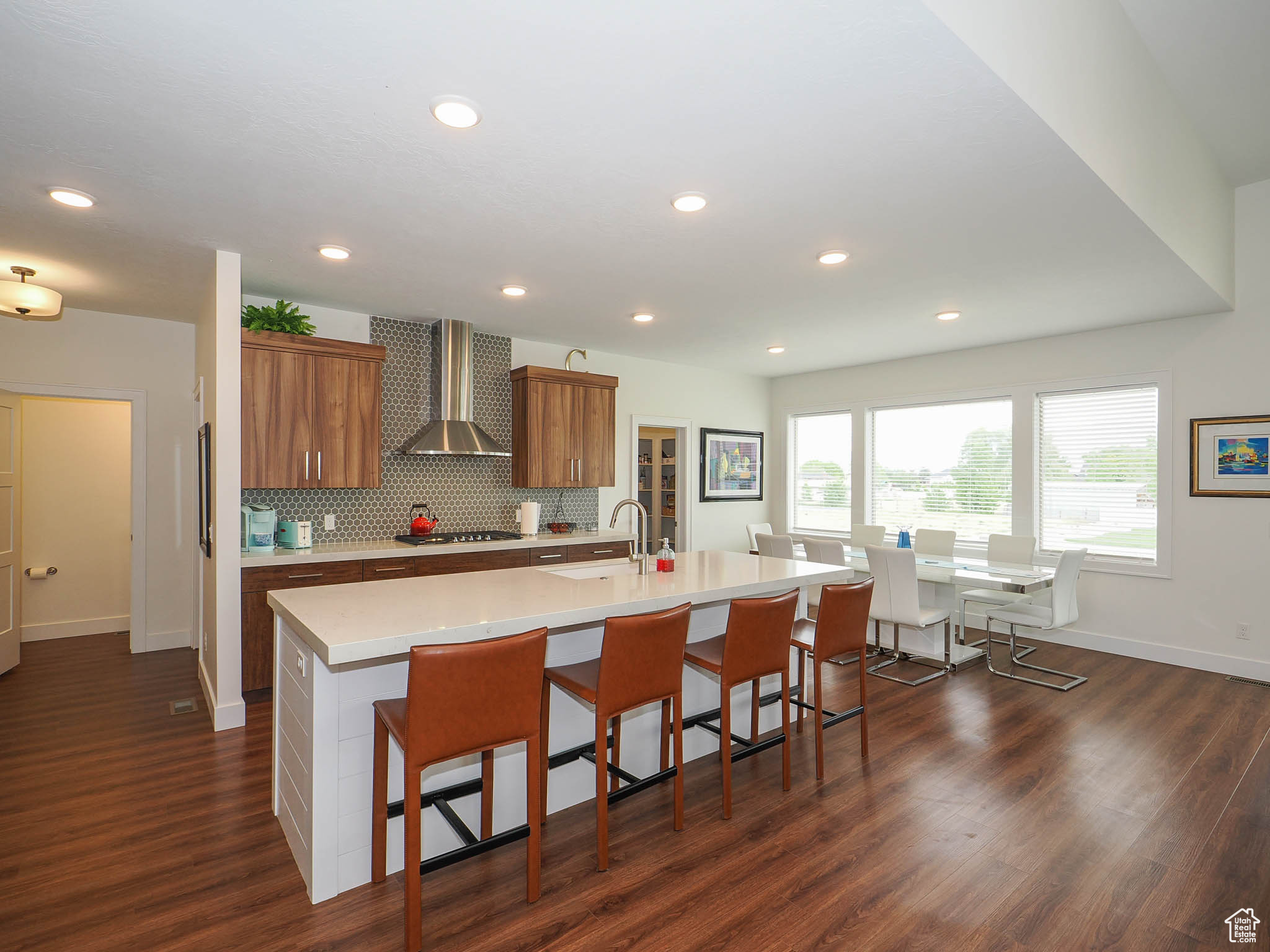 Kitchen with a kitchen breakfast bar, wall chimney range hood, an island with sink, dark hardwood / wood-style flooring, and stainless steel gas cooktop
