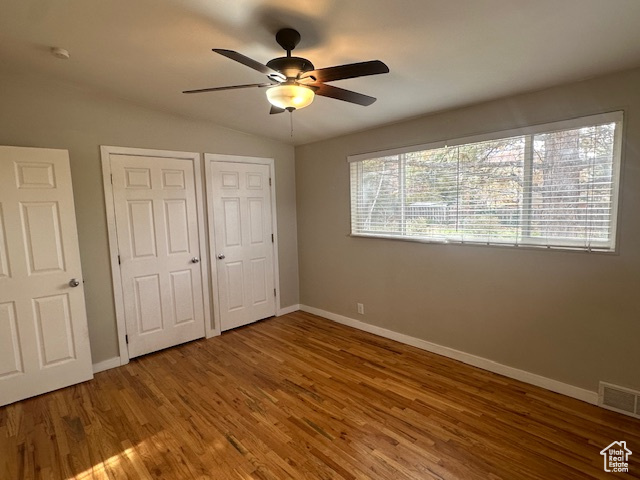 Unfurnished bedroom with hardwood / wood-style floors, lofted ceiling, ceiling fan, and multiple closets