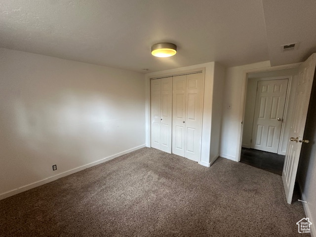 Unfurnished bedroom featuring dark carpet and a closet