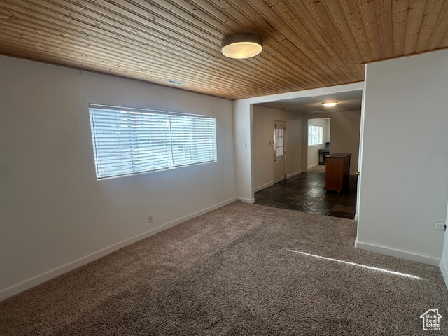 Unfurnished room featuring wood ceiling and dark colored carpet