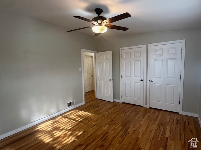 Unfurnished bedroom featuring hardwood / wood-style floors, ceiling fan, and multiple closets