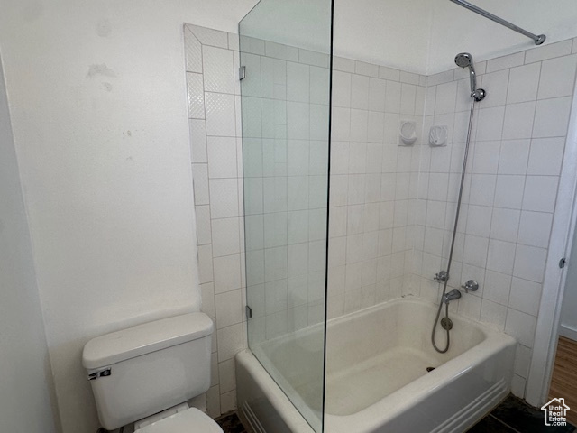 Bathroom with tiled shower / bath combo, toilet, and wood-type flooring