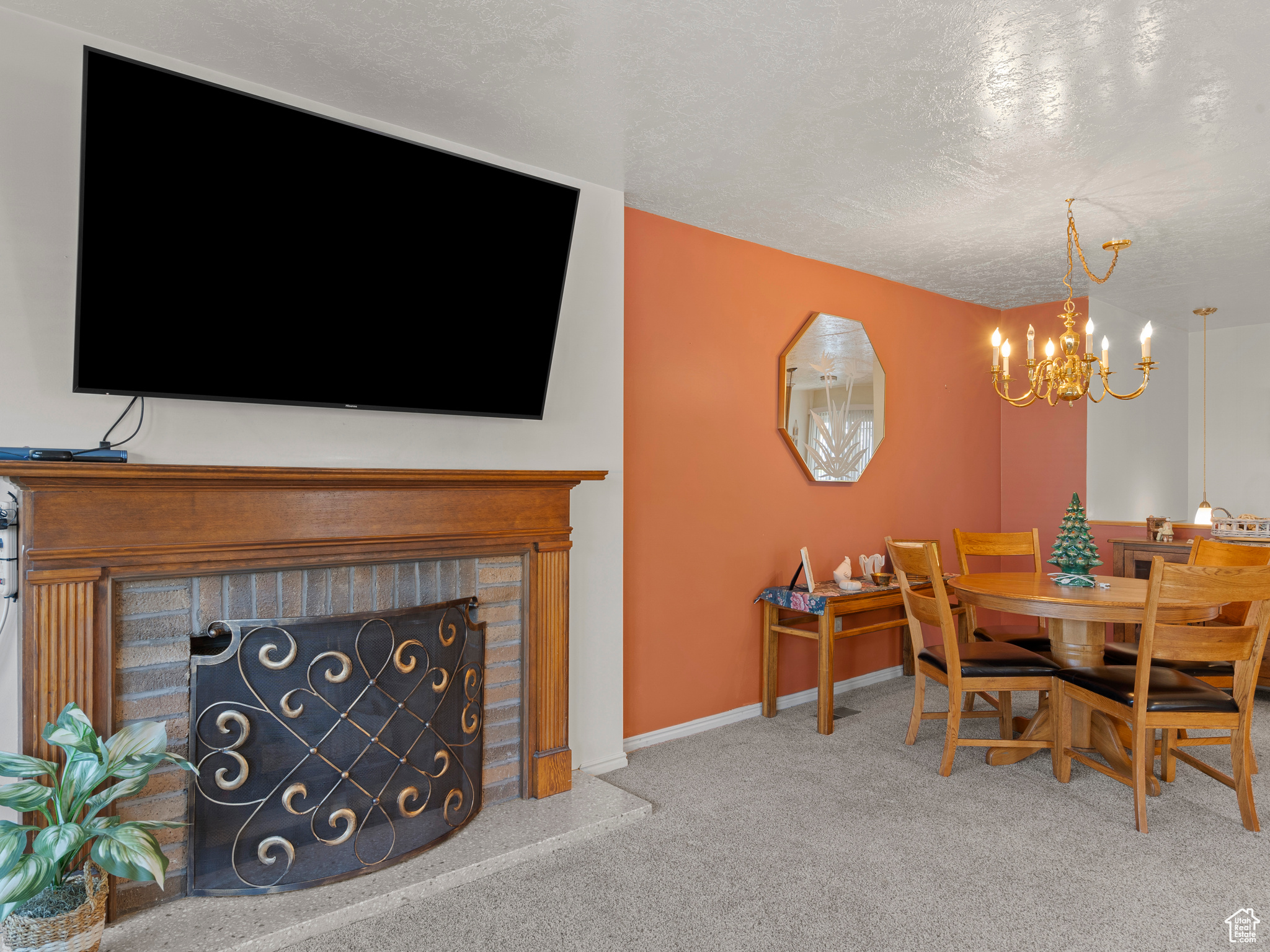 Dining room with carpet flooring, an inviting chandelier, a textured ceiling, and a brick fireplace