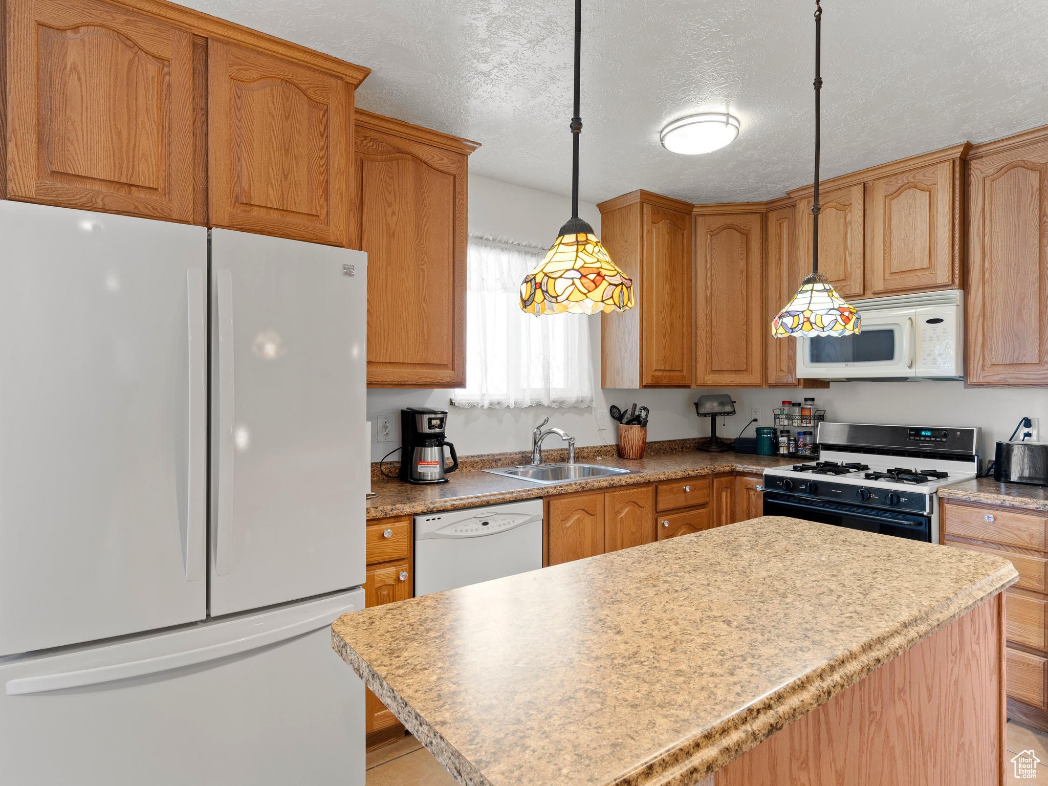 Kitchen with a textured ceiling, sink, decorative light fixtures, and white appliances