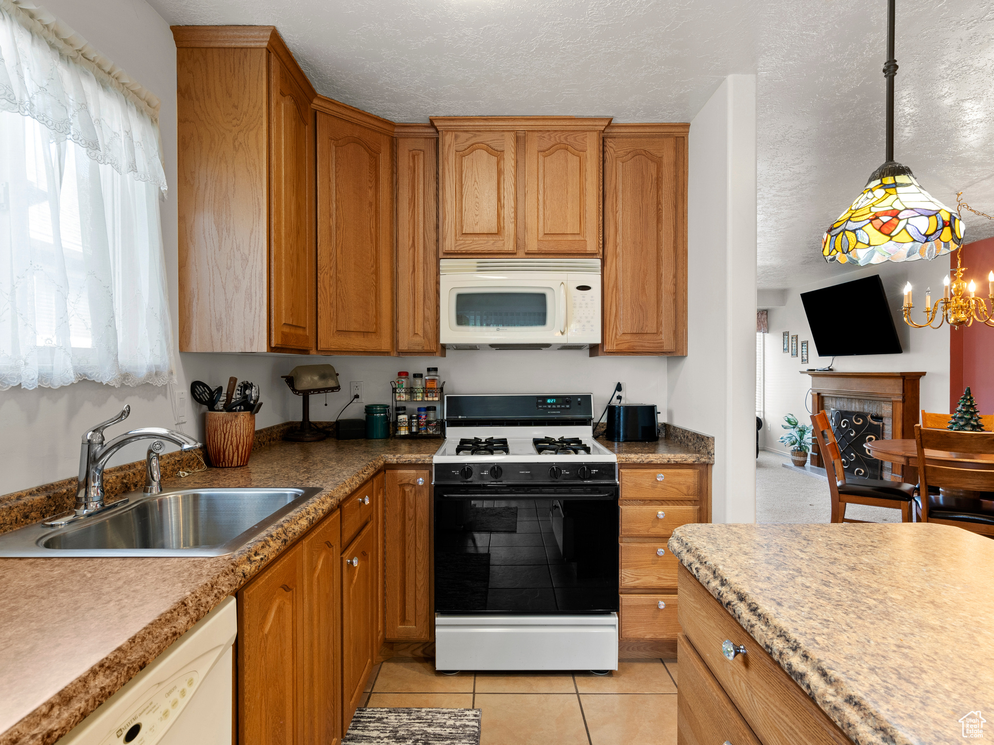 Kitchen featuring white appliances, sink, light tile patterned floors, an inviting chandelier, and a tiled fireplace