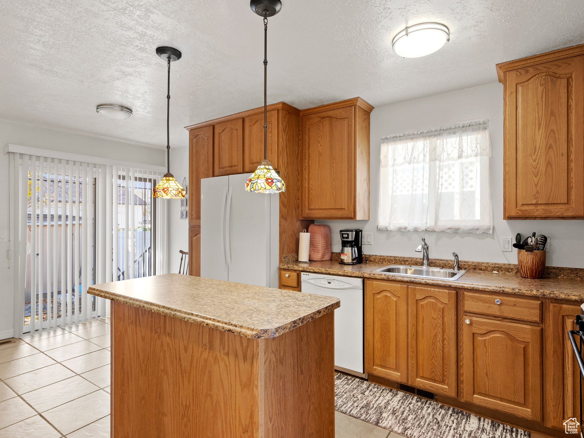 Kitchen featuring a center island, white appliances, sink, light tile patterned floors, and decorative light fixtures