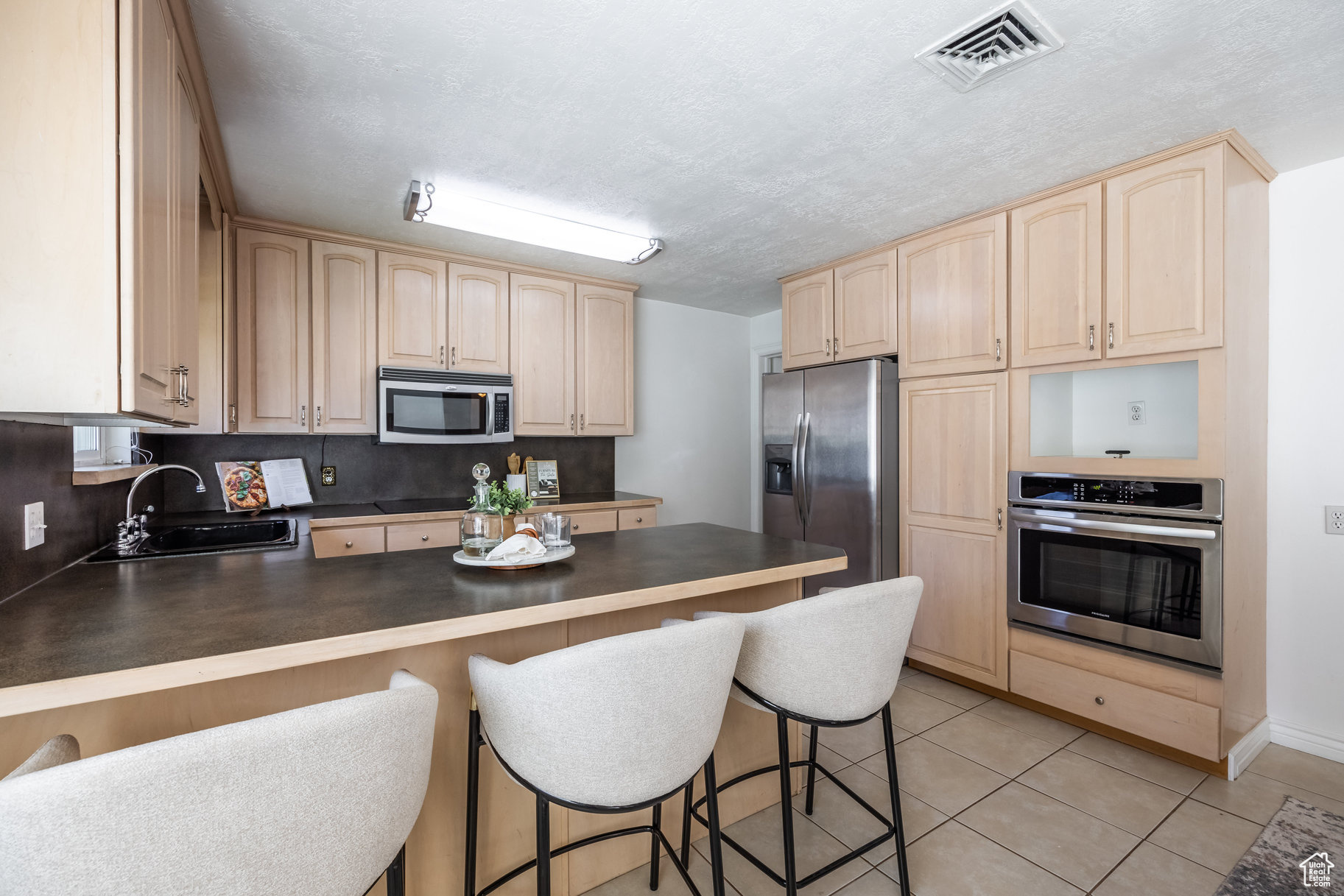 Kitchen with a breakfast bar, sink, light tile patterned floors, kitchen peninsula, and stainless steel appliances