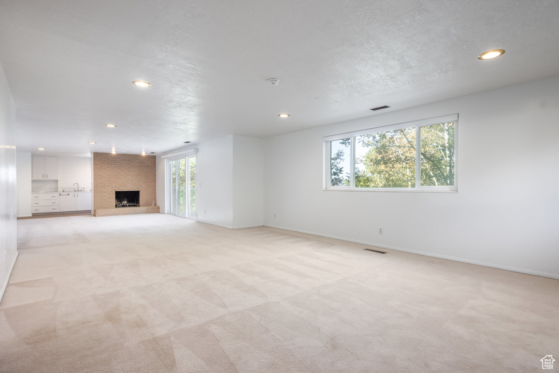 Unfurnished living room with light carpet, a fireplace, a healthy amount of sunlight, and a textured ceiling