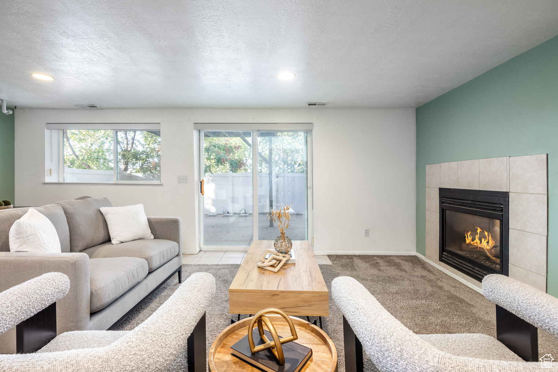 Living room featuring a tile fireplace, light carpet, a textured ceiling, and plenty of natural light