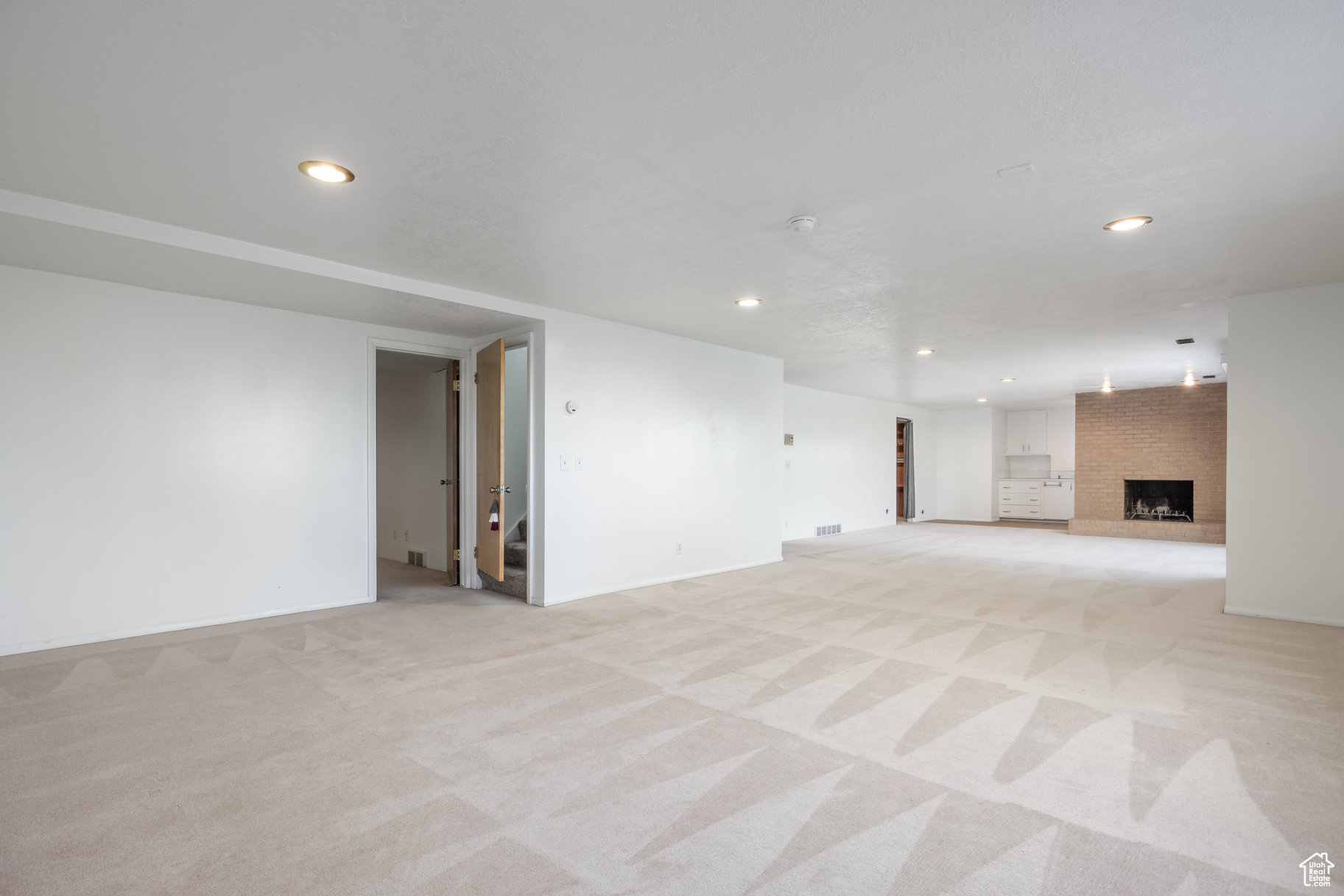 Unfurnished living room featuring light carpet and a brick fireplace