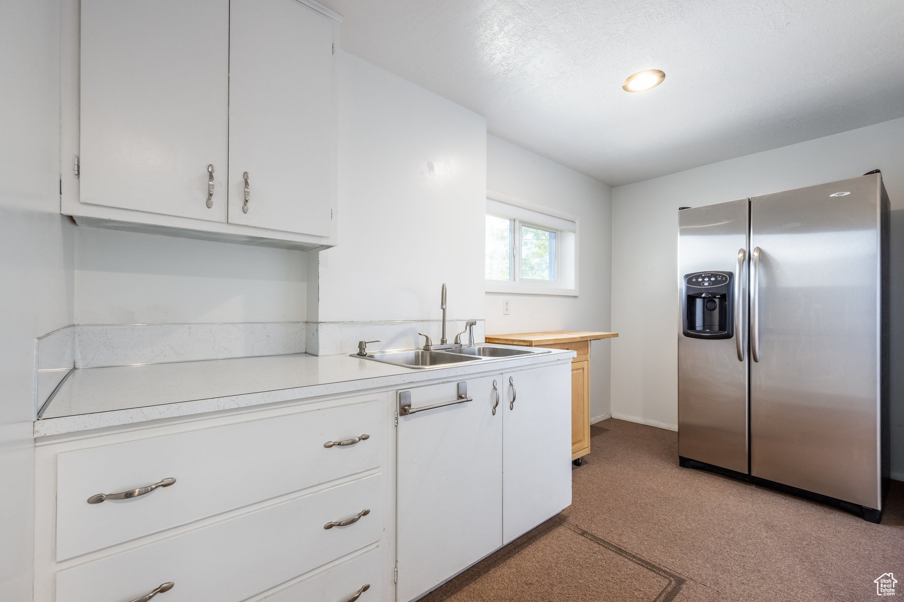 Kitchen featuring sink, white cabinetry, and stainless steel refrigerator with ice dispenser