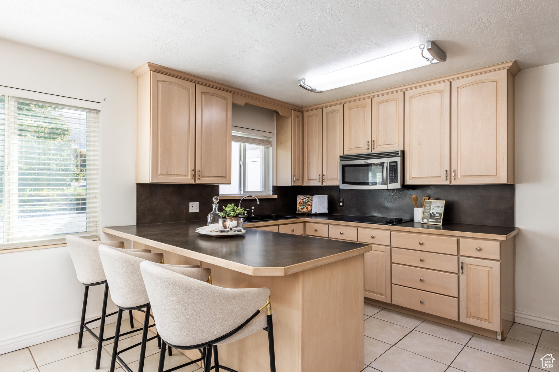 Kitchen featuring kitchen peninsula, a kitchen breakfast bar, backsplash, a textured ceiling, and light brown cabinets